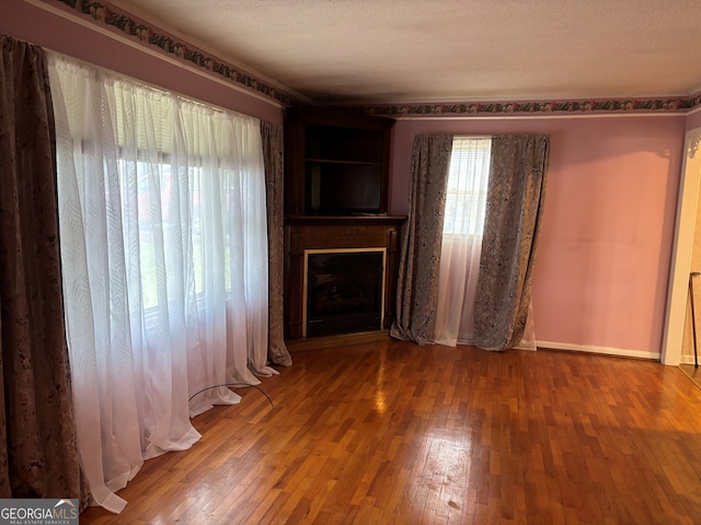 unfurnished living room featuring baseboards, a fireplace, a textured ceiling, and hardwood / wood-style floors