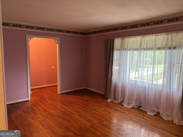 empty room featuring baseboards, a textured ceiling, and wood finished floors