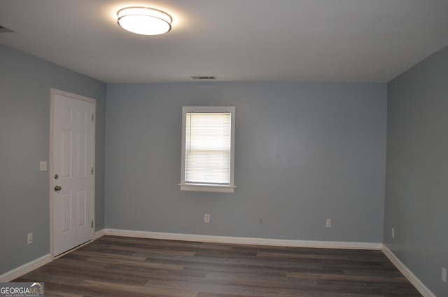 empty room featuring visible vents, dark wood finished floors, and baseboards