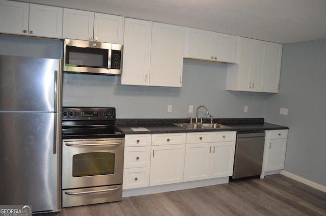 kitchen with a sink, stainless steel appliances, dark wood finished floors, and white cabinetry