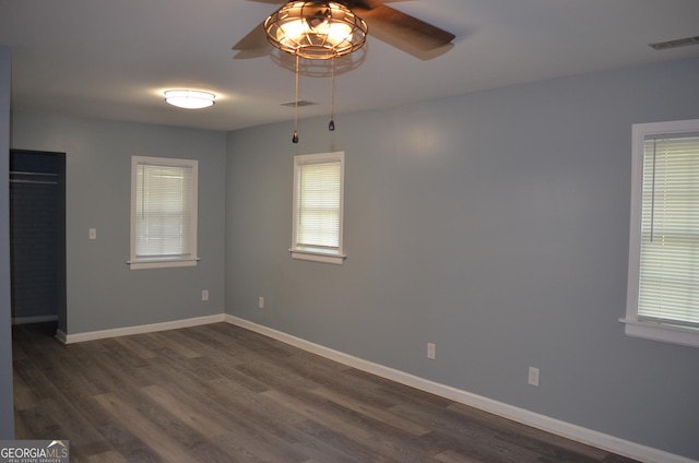 spare room featuring a healthy amount of sunlight, a ceiling fan, dark wood-style flooring, and visible vents