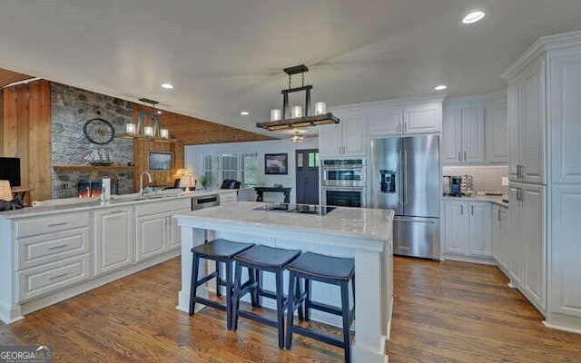 kitchen with appliances with stainless steel finishes, white cabinets, vaulted ceiling, and a kitchen breakfast bar