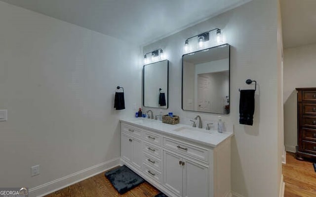 full bath featuring baseboards, a sink, wood finished floors, and double vanity