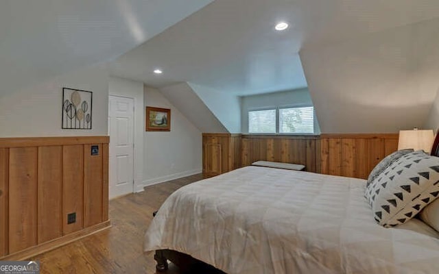 bedroom featuring wooden walls, wainscoting, wood finished floors, and lofted ceiling