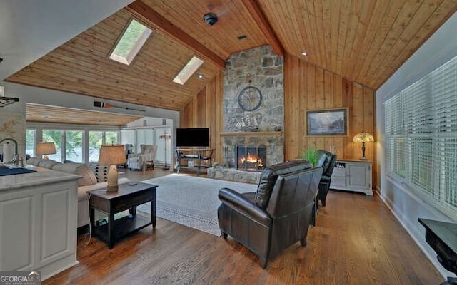 living area with wood finished floors, a stone fireplace, high vaulted ceiling, wooden ceiling, and a skylight