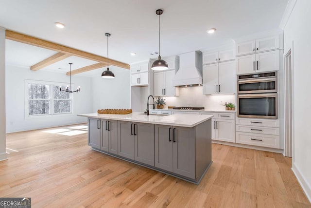 kitchen with a sink, light countertops, custom exhaust hood, stainless steel appliances, and light wood-style flooring