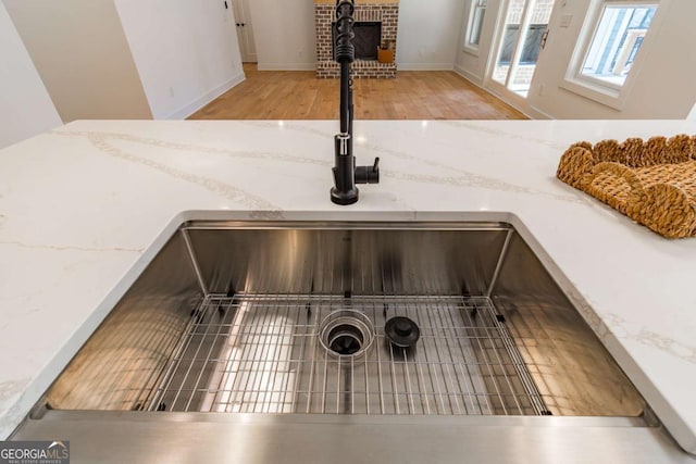 interior details featuring a sink, light stone counters, a fireplace, and wood finished floors