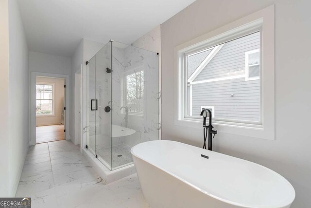 bathroom featuring baseboards, marble finish floor, a marble finish shower, and a soaking tub