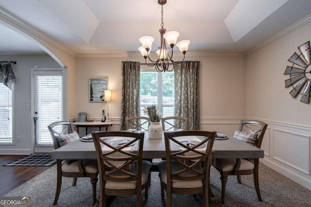 dining space featuring arched walkways, wood finished floors, a raised ceiling, an inviting chandelier, and ornamental molding