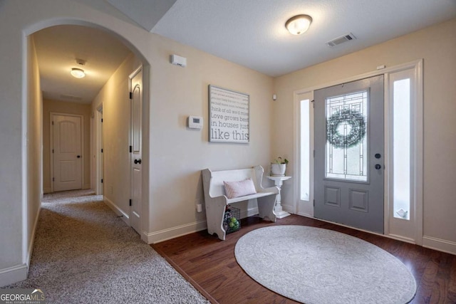 entrance foyer featuring arched walkways, baseboards, visible vents, and wood finished floors