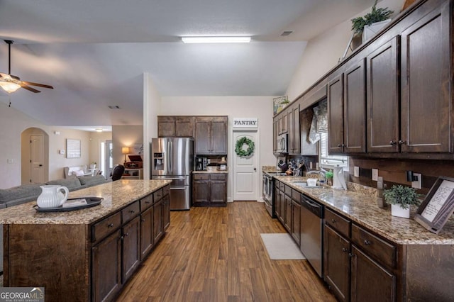 kitchen with dark brown cabinetry, arched walkways, a ceiling fan, dark wood finished floors, and appliances with stainless steel finishes