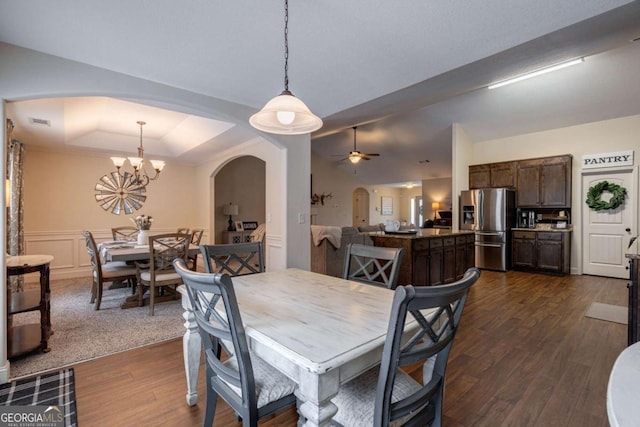 dining space with visible vents, arched walkways, dark wood finished floors, ceiling fan with notable chandelier, and a tray ceiling