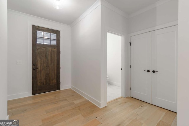foyer with light wood-style floors, ornamental molding, and baseboards