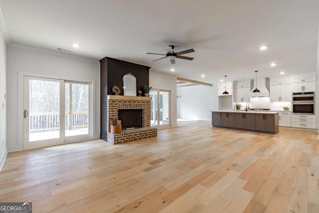 unfurnished living room featuring crown molding, a ceiling fan, a wealth of natural light, and light wood-style floors