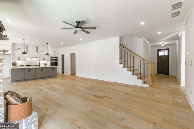 unfurnished living room with a ceiling fan, visible vents, stairway, baseboards, and light wood-style flooring