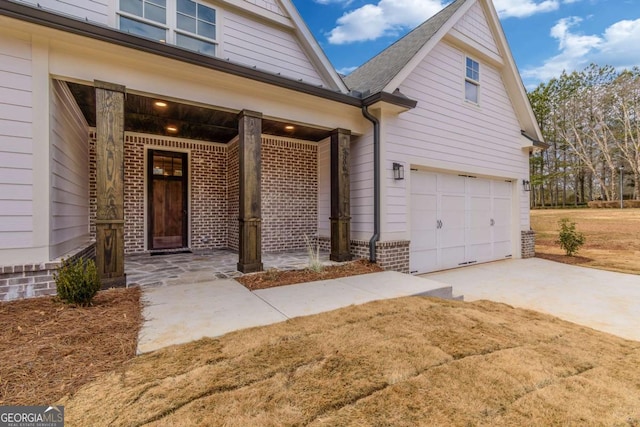 doorway to property with an attached garage, driveway, brick siding, and a porch