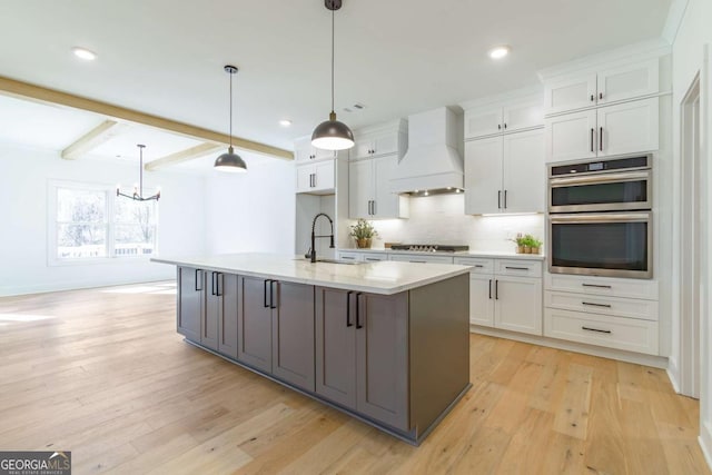 kitchen featuring a sink, premium range hood, light countertops, an inviting chandelier, and white cabinetry