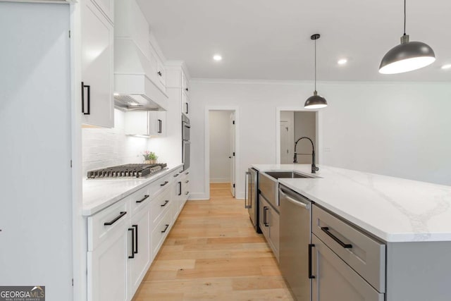 kitchen with a kitchen island with sink, light stone countertops, a sink, light wood-style flooring, and appliances with stainless steel finishes