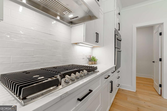 kitchen featuring light wood-style floors, stainless steel appliances, white cabinetry, decorative backsplash, and custom exhaust hood
