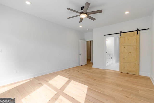 unfurnished bedroom with light wood-type flooring, a barn door, baseboards, and recessed lighting