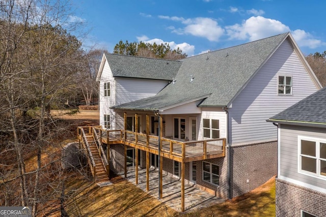 back of house with brick siding, a shingled roof, stairway, and a deck