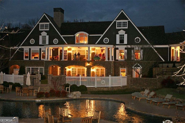 back of house at night featuring a patio, fence, and a chimney