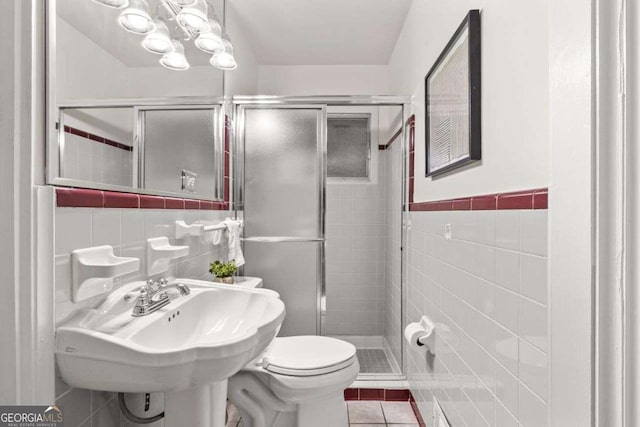 bathroom featuring toilet, tile patterned floors, tile walls, and a shower stall