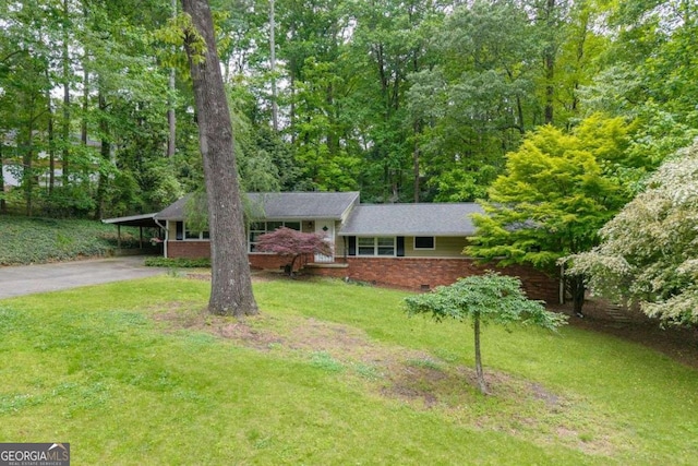 ranch-style home featuring a front lawn, brick siding, driveway, a wooded view, and a carport