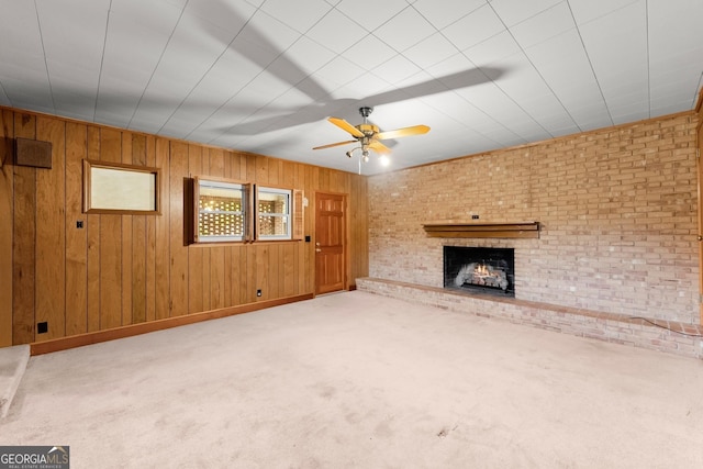 unfurnished living room with wooden walls, carpet floors, a fireplace, and a ceiling fan