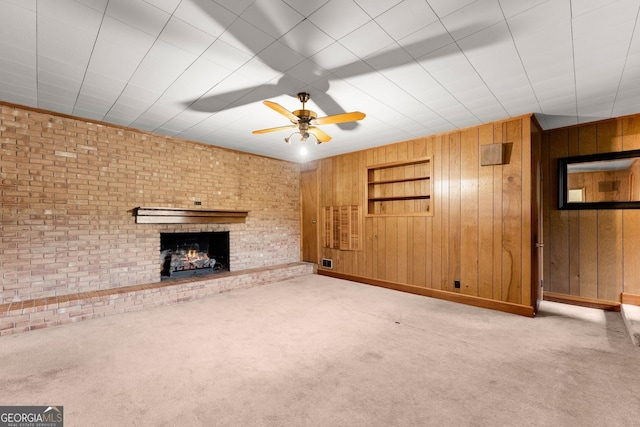 unfurnished living room with a ceiling fan, carpet, a brick fireplace, and wood walls