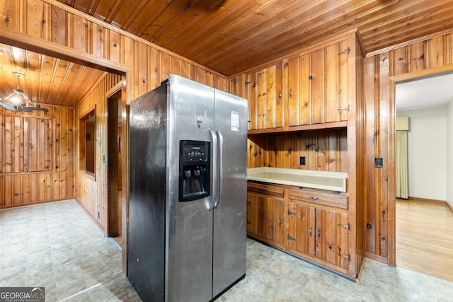 kitchen featuring wooden walls, stainless steel fridge with ice dispenser, and light floors