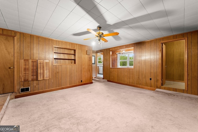 unfurnished living room featuring visible vents, carpet floors, baseboards, wooden walls, and a ceiling fan