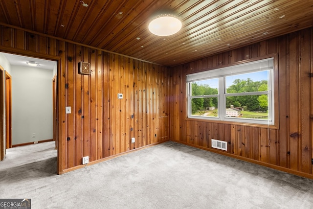 empty room with visible vents, wood walls, wooden ceiling, baseboards, and carpet