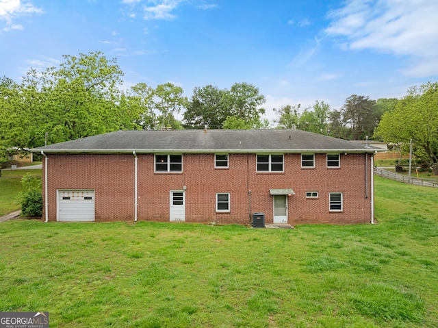 back of house with a lawn, brick siding, central AC, and an attached garage