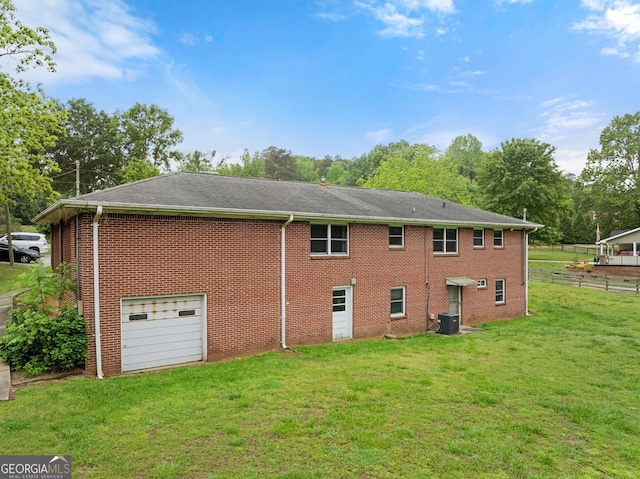 back of property with an attached garage, brick siding, central air condition unit, a lawn, and driveway