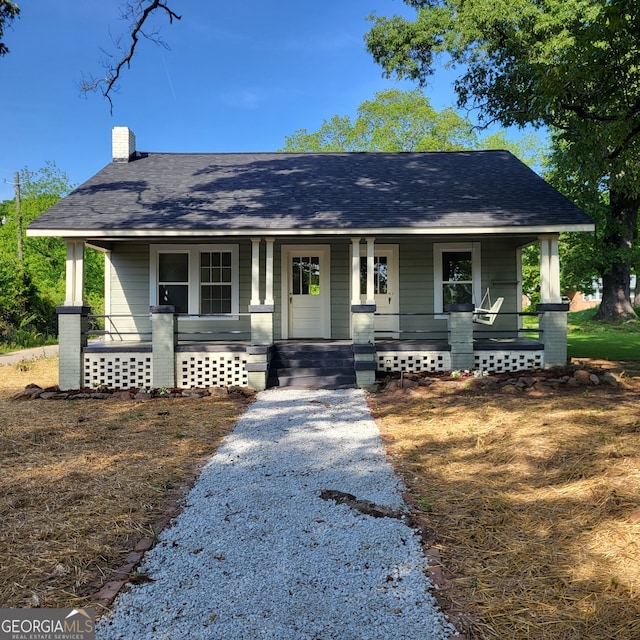 view of front of property featuring roof with shingles, a chimney, and a porch