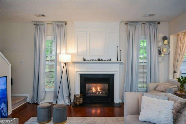interior space with a glass covered fireplace, baseboards, wood finished floors, and visible vents