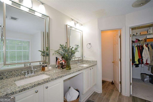 full bathroom with double vanity, visible vents, a sink, and wood finished floors