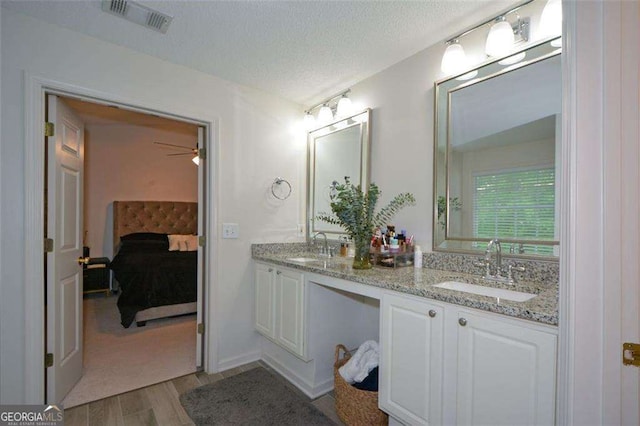 ensuite bathroom featuring visible vents, a sink, wood finished floors, and double vanity