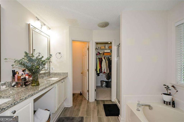 full bathroom with double vanity, a garden tub, a textured ceiling, a sink, and a spacious closet