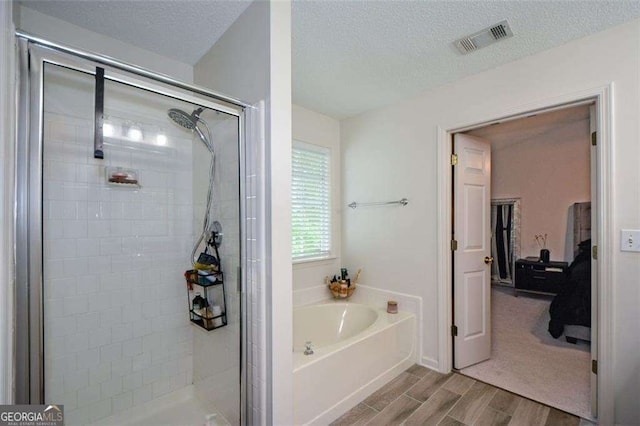 full bathroom with visible vents, wood finish floors, a textured ceiling, a bath, and a stall shower