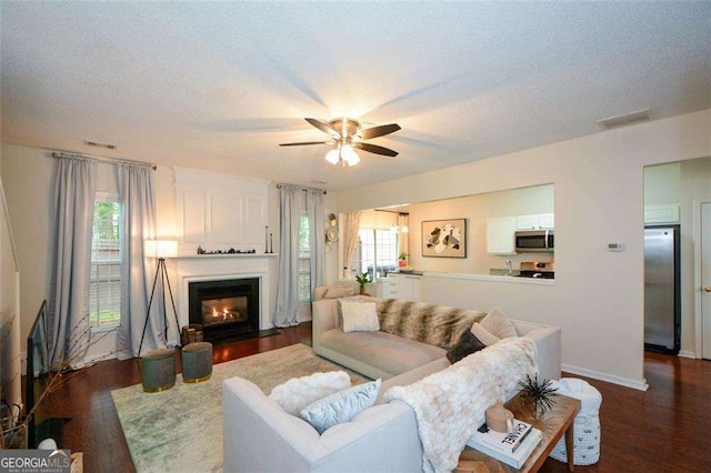 living room featuring plenty of natural light, ceiling fan, dark wood-style floors, and visible vents