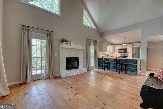 living room with a fireplace, high vaulted ceiling, baseboards, and light wood-type flooring