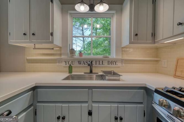kitchen featuring light countertops, stainless steel gas range, tasteful backsplash, and a sink