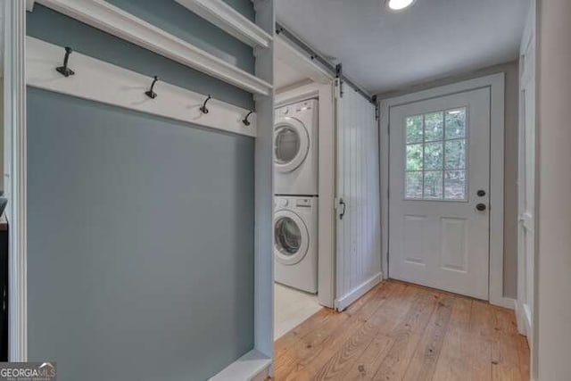 washroom featuring light wood finished floors, laundry area, stacked washer / drying machine, and a barn door