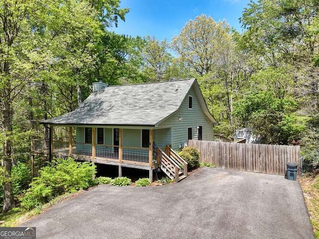 rustic home with fence, covered porch, a chimney, and roof with shingles