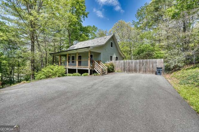 view of front facade with a chimney, fence, covered porch, and driveway