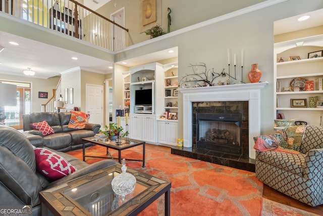 living area with built in features, a tile fireplace, ornamental molding, a high ceiling, and stairs
