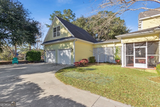 view of side of home with a lawn, concrete driveway, a sunroom, and a garage