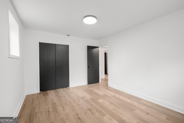 unfurnished bedroom featuring baseboards, light wood-style flooring, and a closet